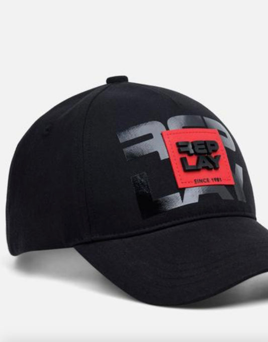 A black baseball cap featuring a large black and gray graphic on the front panel and a bright red rectangular patch with the black text 'REPLAY' 