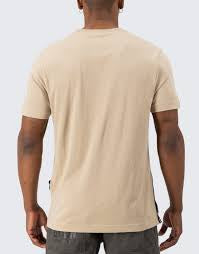 A man viewed from the back wearing a light beige crew-neck t-shirt and dark gray pants, set against a plain light gray background.
